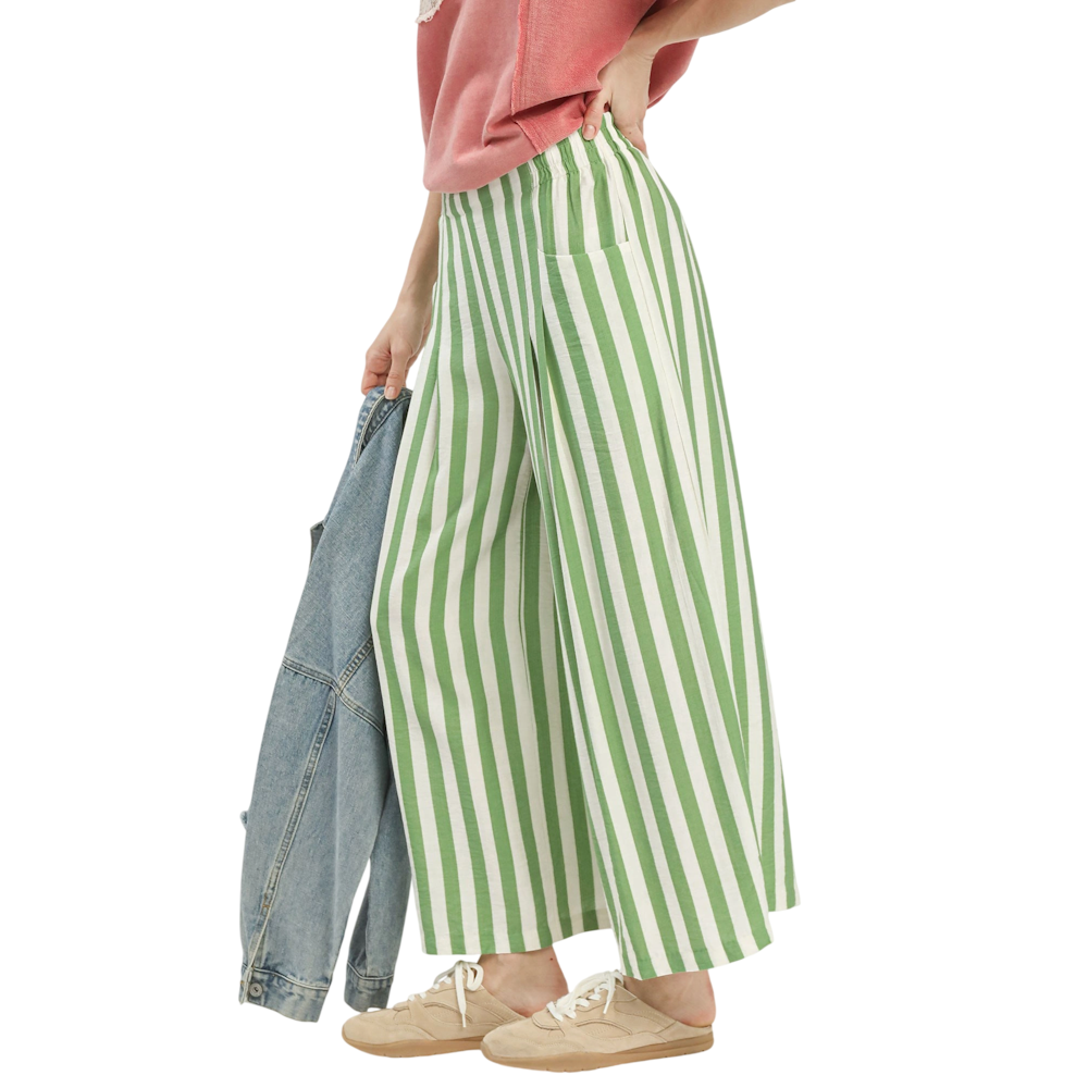 A person wearing wide-leg pants with green and white vertical stripes, tan sneakers, and a pink shirt.