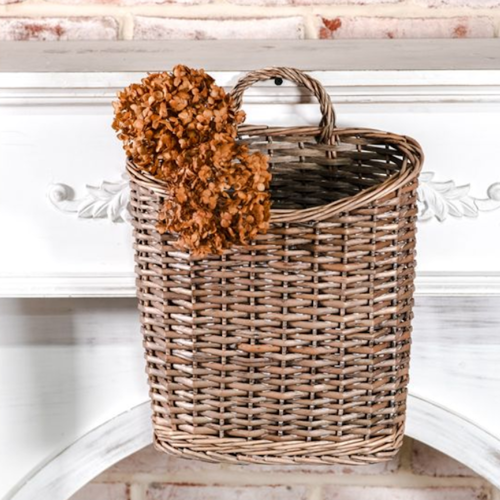 Grey woven willow hanging basket with dried brown florals hanging against a white wooden mantle.