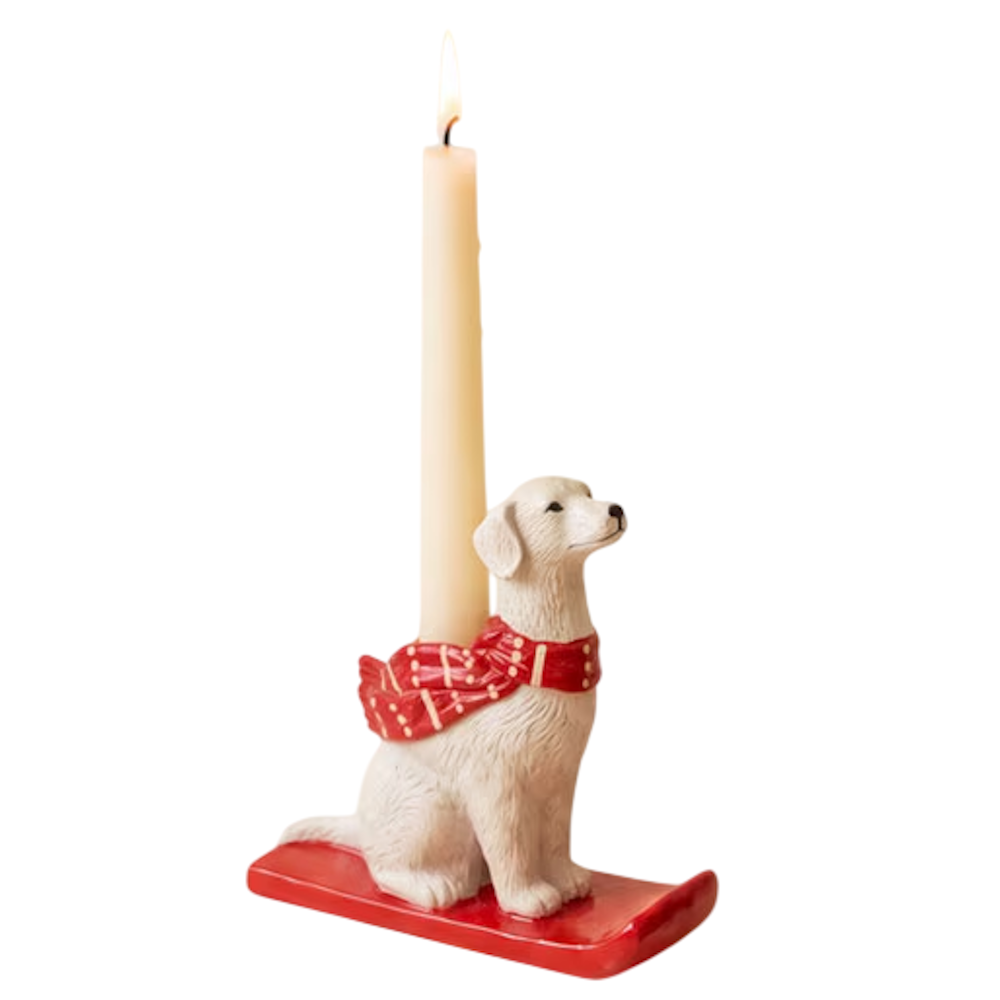 Ceramic white dog taper candleholder wearing a red pattern scarf on a red sled.