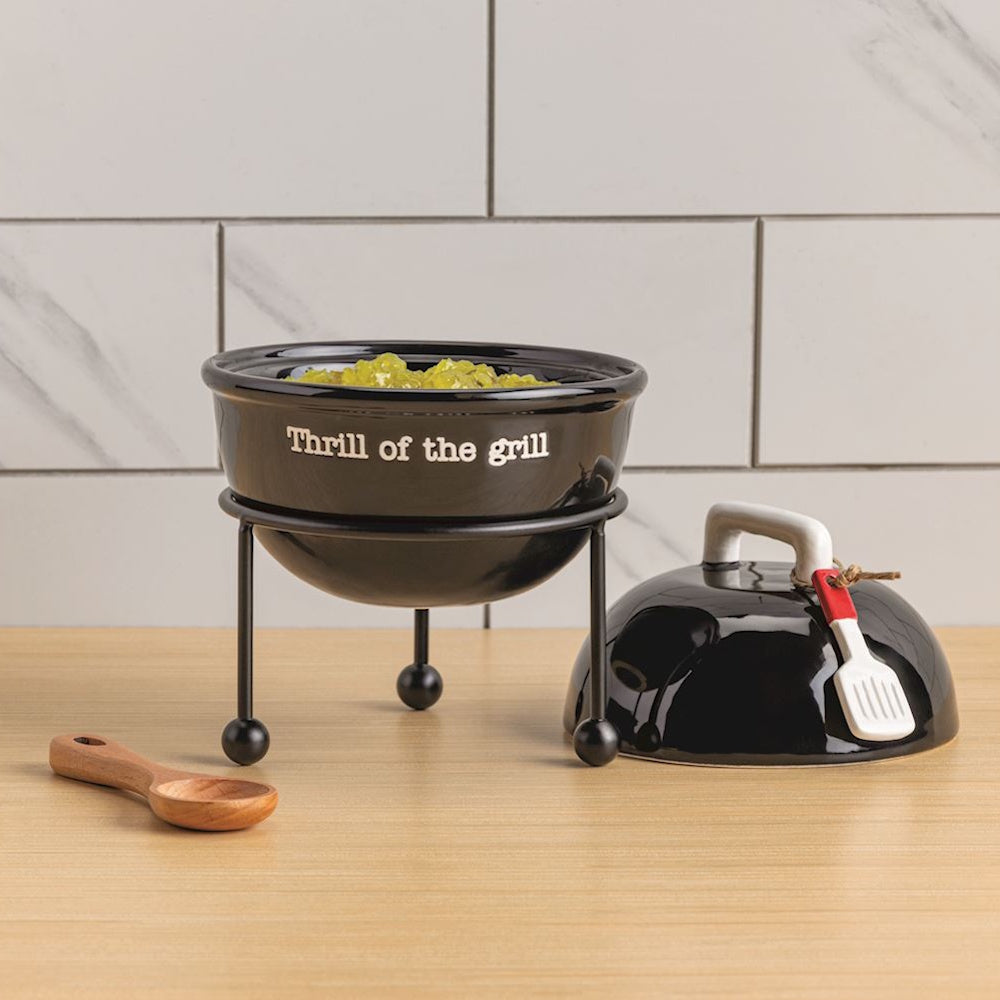 Black ceramic grill-shaped serving bowl on a stand with lid and 'Thrill of the grill' text.