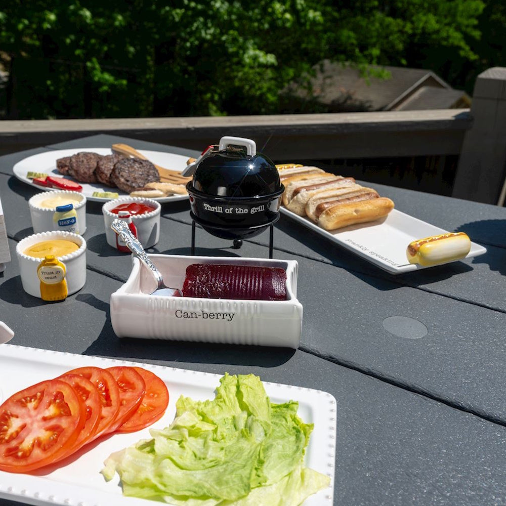 Summer barbecue spread with grilled burgers, hot dogs, and condiments on a patio table.