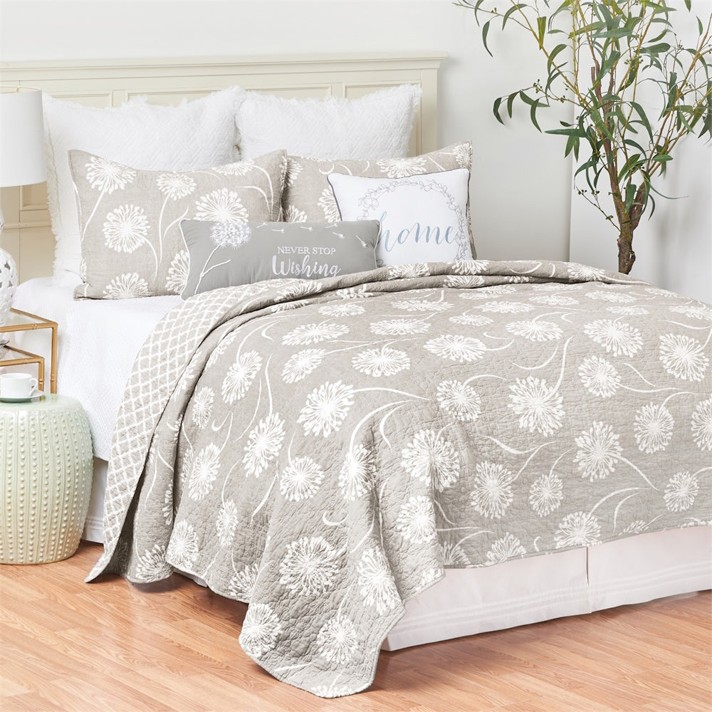 A bed styled with a grey and white floral dandelion quilt, matching shams, and decorative pillows.