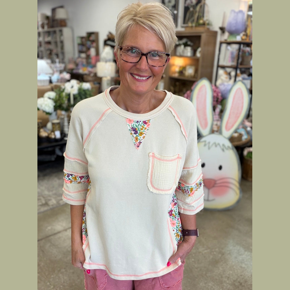 Woman wearing cream floral patchwork top and pink shorts in a home decor shop.