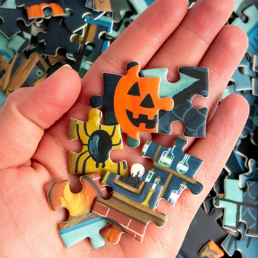 Hand holding colorful Halloween puzzle pieces with a jack-o'-lantern, spider, and potion bottles.