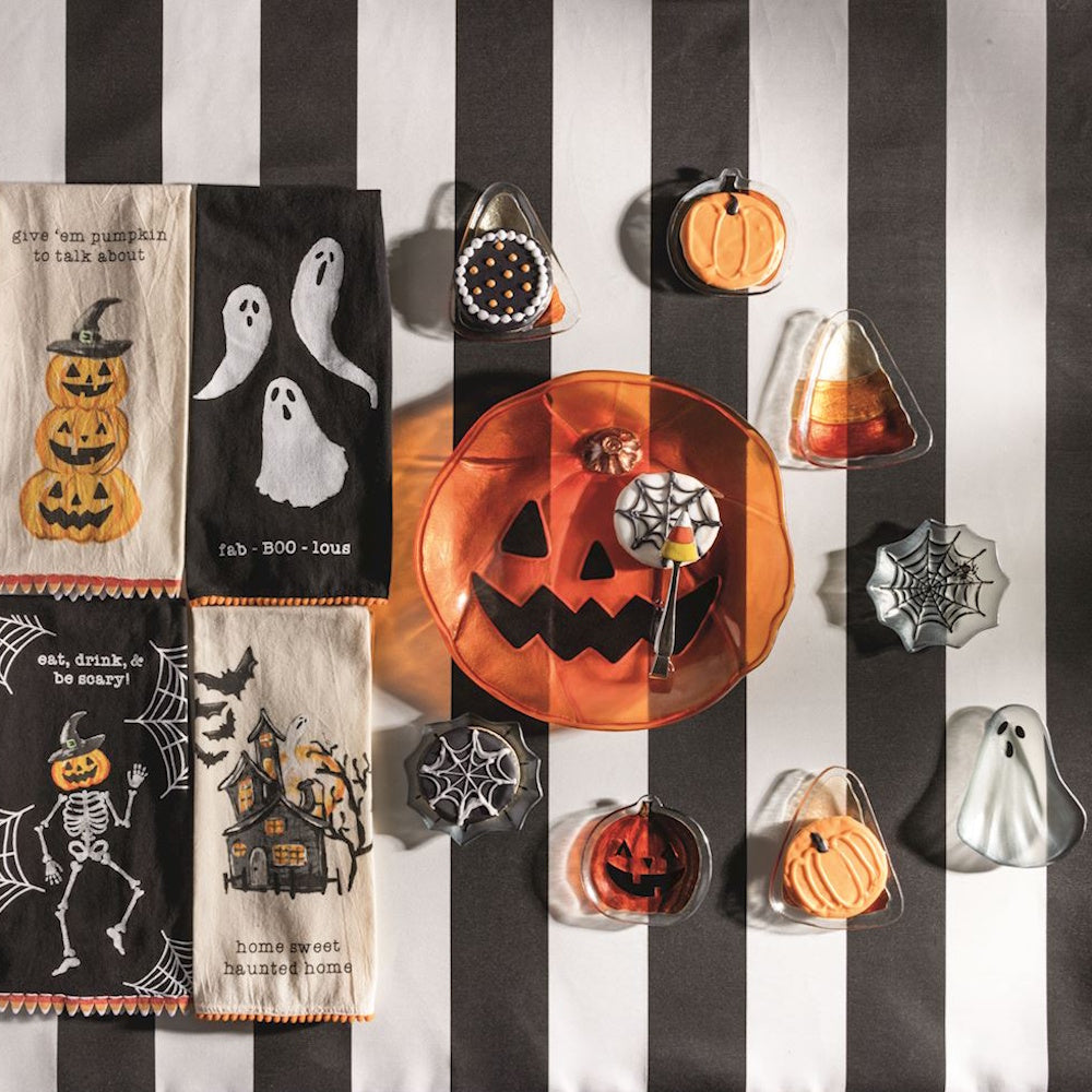 Halloween tidbit plates, pumpkin platter, and themed dish towels on a black and white striped background.