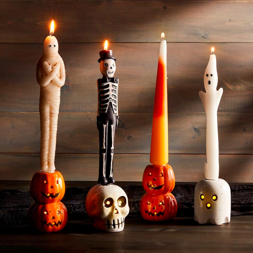 Spooky Halloween taper candles shaped like a mummy, skeleton, candy corn, and ghost in themed holders.