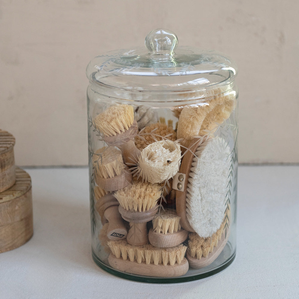 Hand-blown glass jar with etched botanical patterns filled with eco-friendly wooden scrub brushes.
