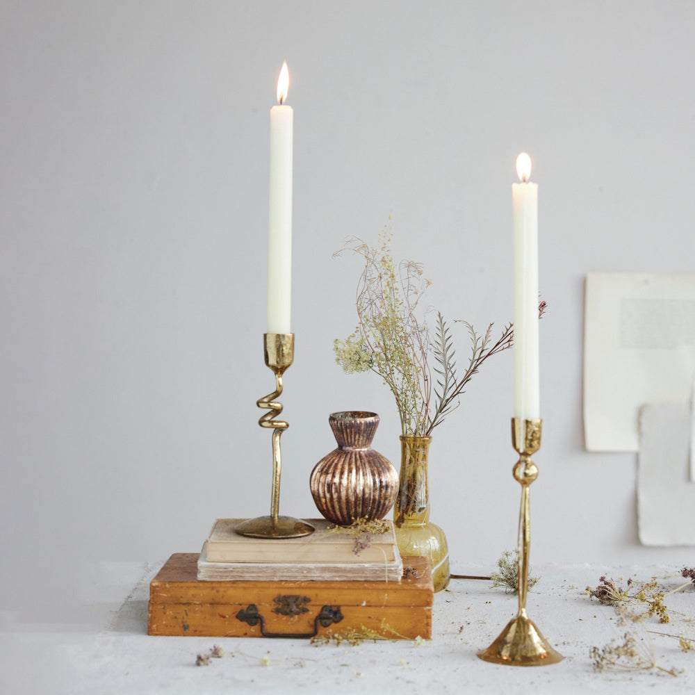 Two gold taper candle holders with lit white candles, styled on stacked books and a wooden box with decor.