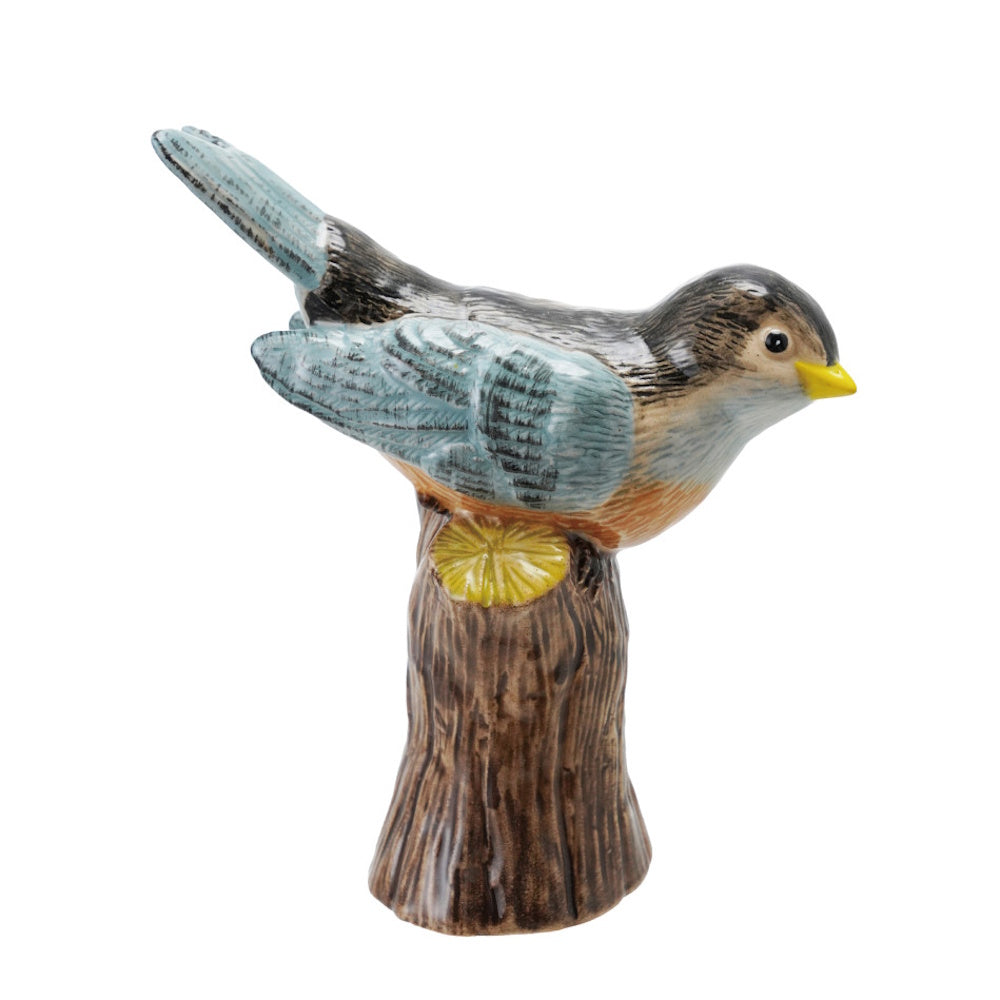 Side view of a hand-painted ceramic bird figurine perched on a brown tree stump base.