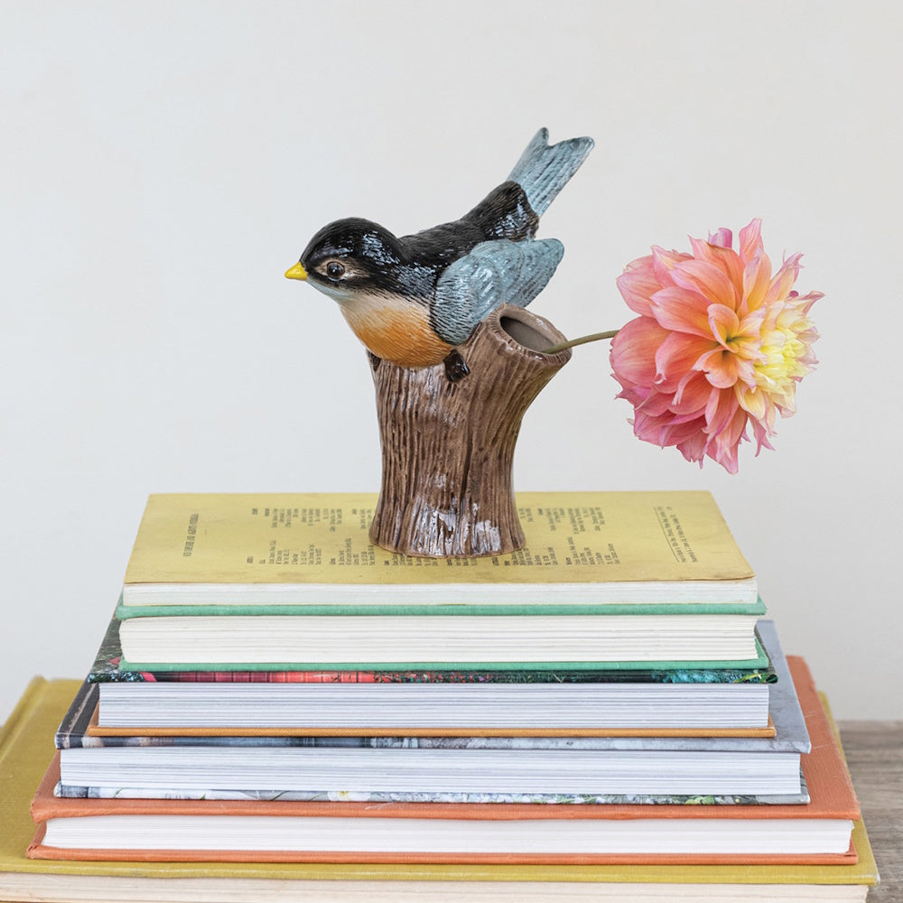 Small ceramic bird vase sitting on a stack of books, holding a single pink and yellow flower.