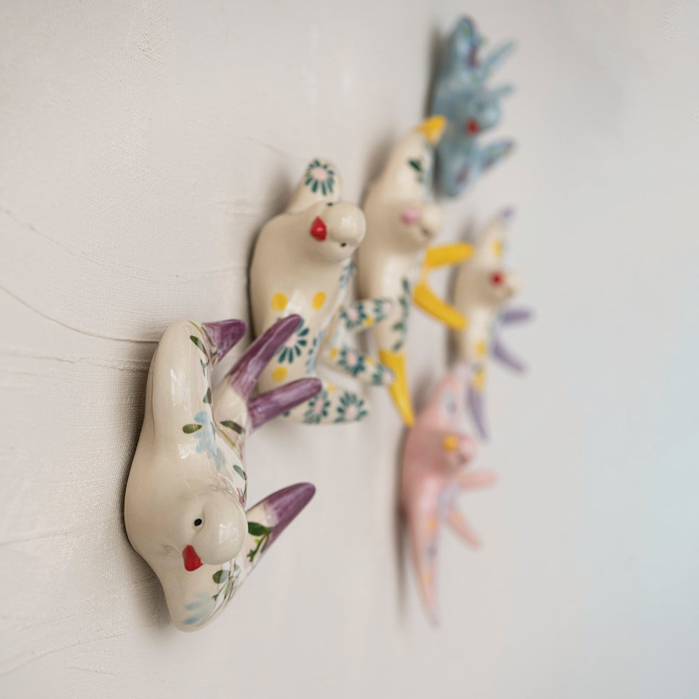 A side view of multiple colorful, hand-painted ceramic bird figurines mounted on a textured white wall.