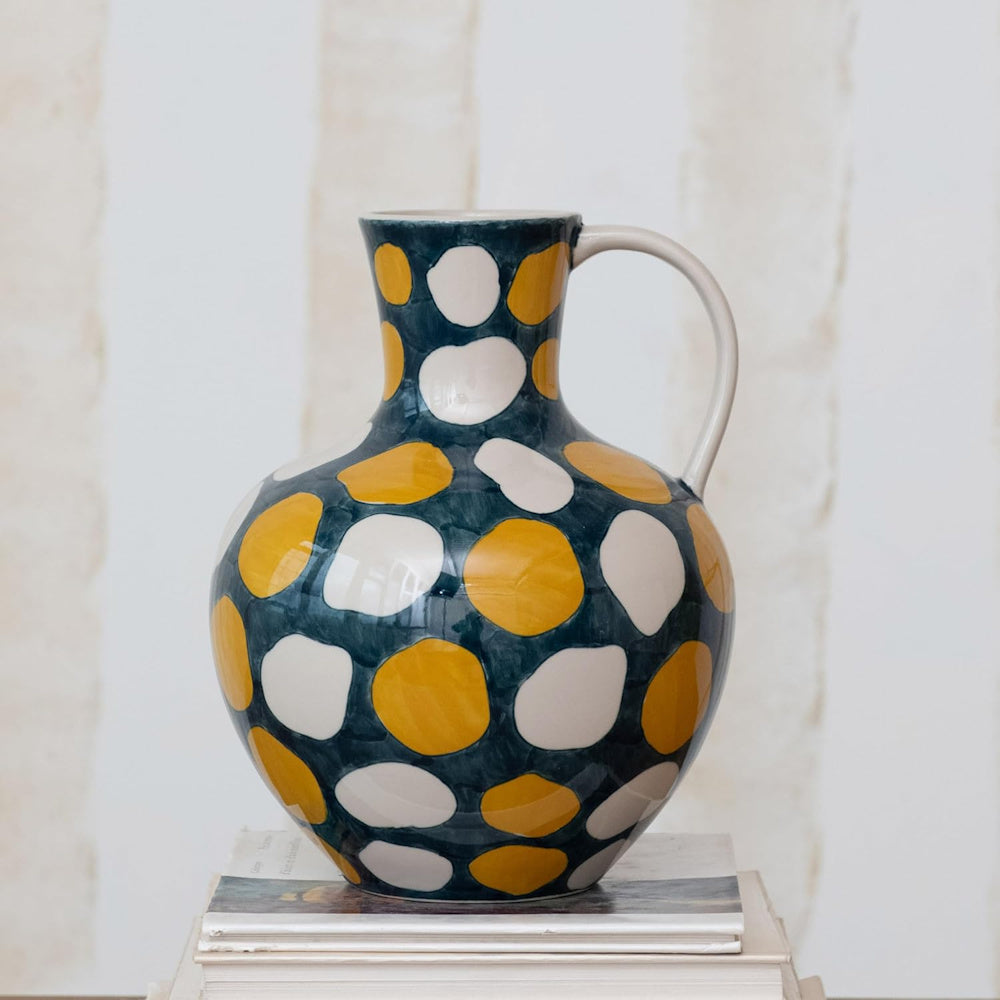 Large ceramic pitcher with yellow and white polka dots on a dark blue base, sitting on a stack of books.