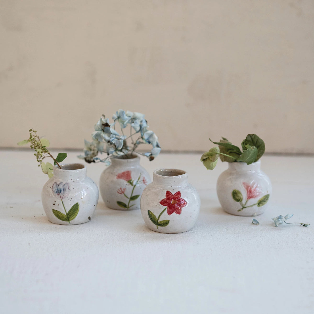 Collection of four small hand-painted stoneware bud vases with floral designs and dried flowers.