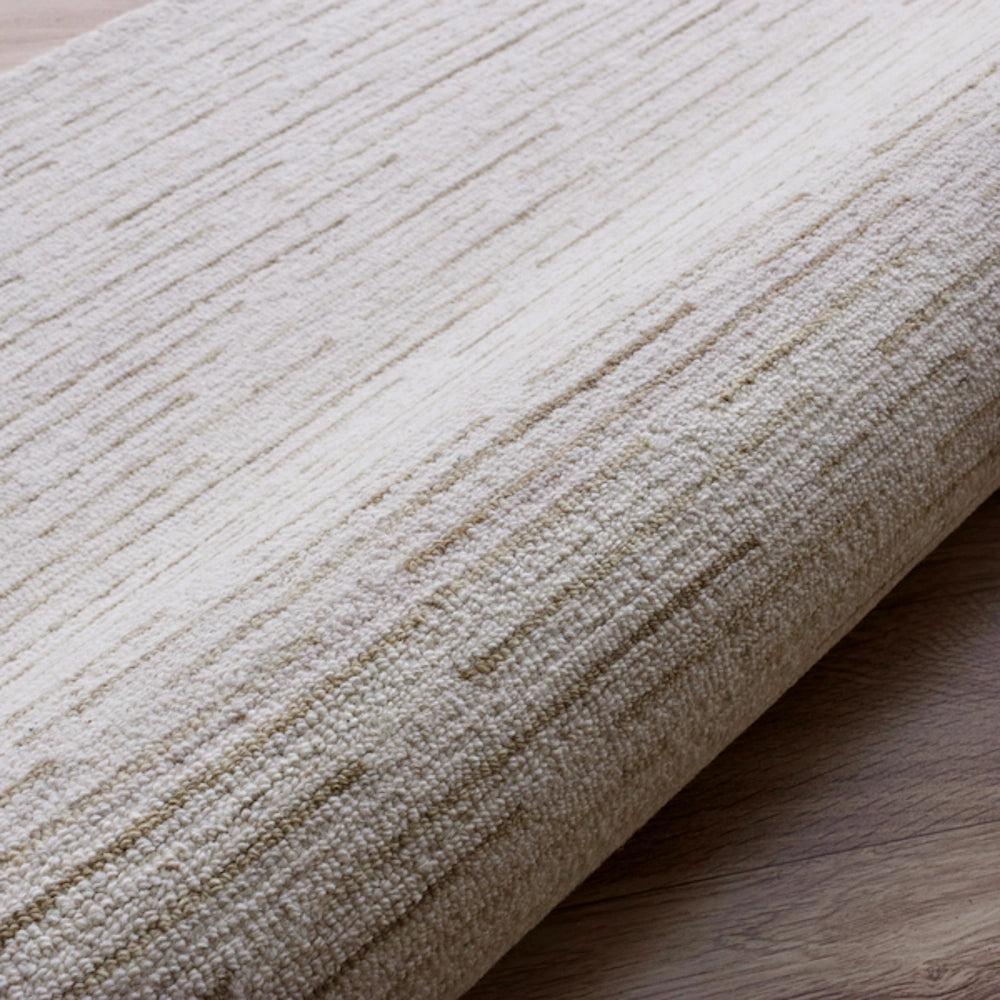 Cream hand tufted rectangle Babylon rug with textured linear patterns on a wooden floor.