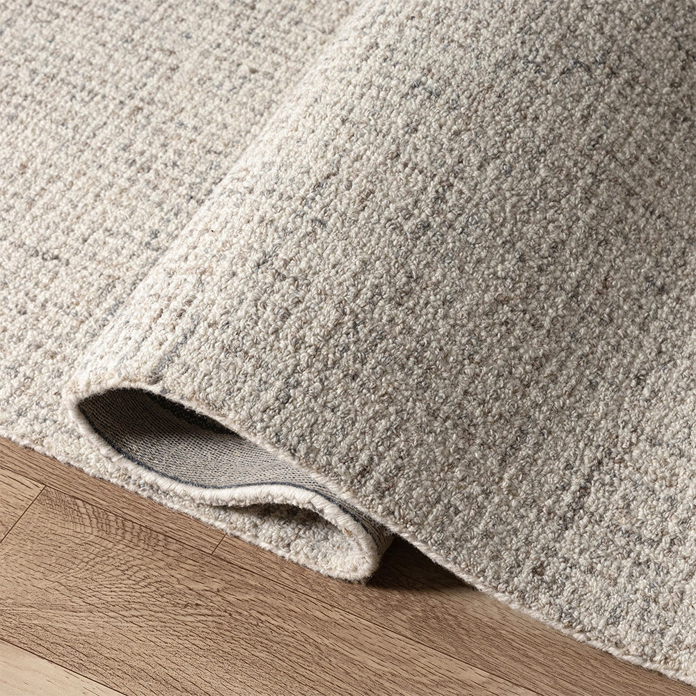 Close-up of a textured cream and grey wool area rug with a looped pile, folded on a light wood floor.