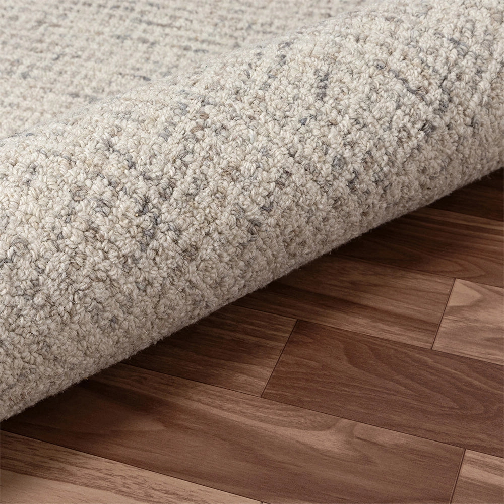 Cream and grey textured loop pile area rug partially rolled on a dark walnut hardwood floor.