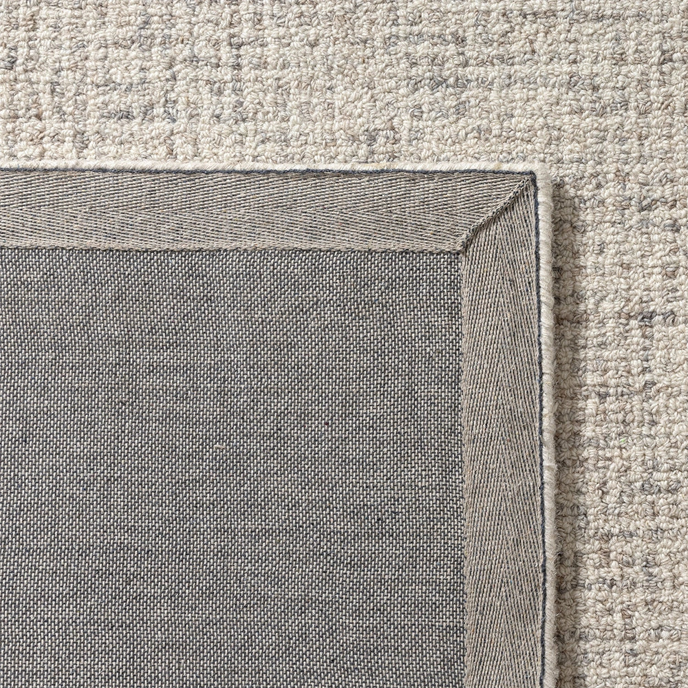 Close-up of the grey canvas backing and durable edge binding on a textured beige wool area rug.