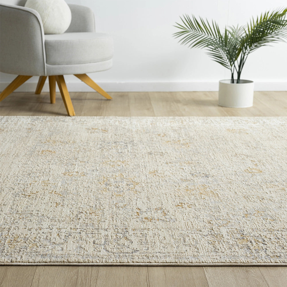 Hand-tufted Monaco rug with a distressed beige and gold pattern in a bright living room with a grey chair and plant.