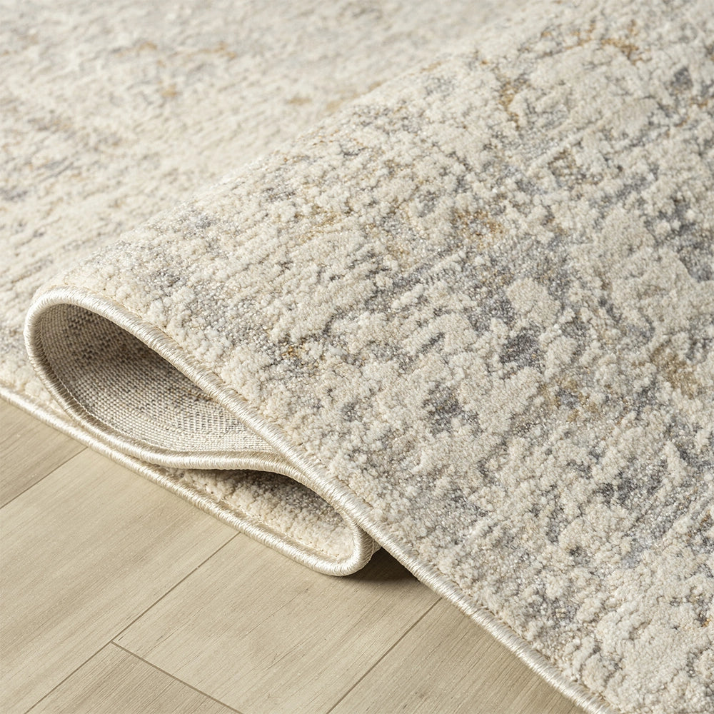 Close-up of a neutral cream and grey textured Monaco rug with a distressed pattern and rolled corner.