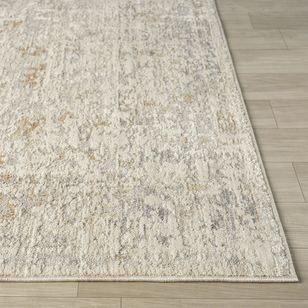 Close-up of a hand-tufted Monaco rug featuring a distressed cream, grey, and gold oriental pattern on light wood flooring.