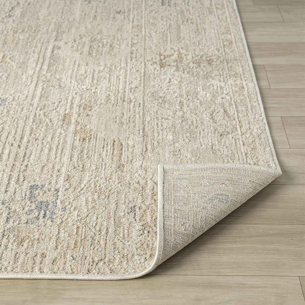Beige and ivory hand-tufted Monaco rug with a distressed pattern and a folded corner showing the backing.