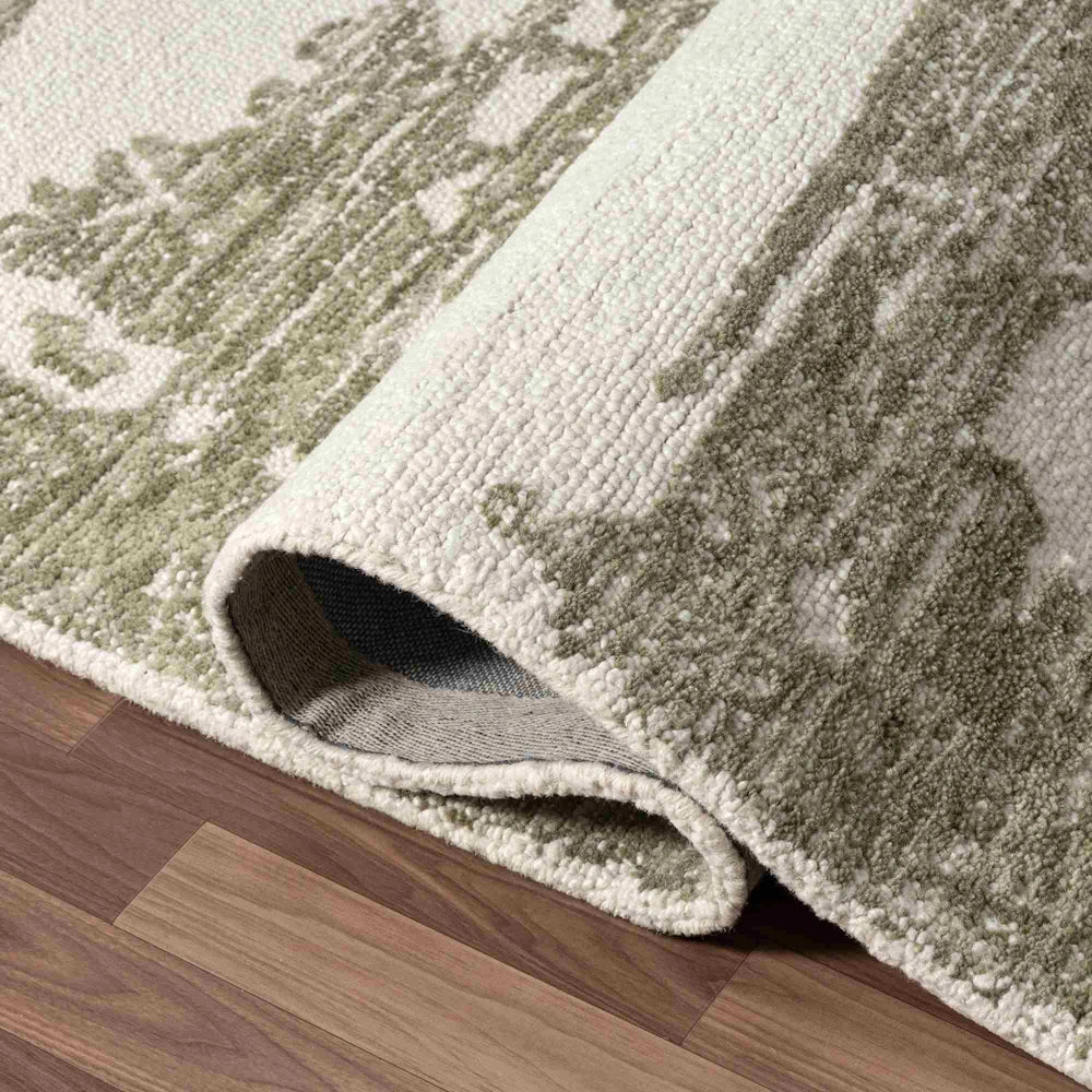 Close up of green and ivory hand tufted rug corner showing textured pile, abstract pattern and folded edge detail.
