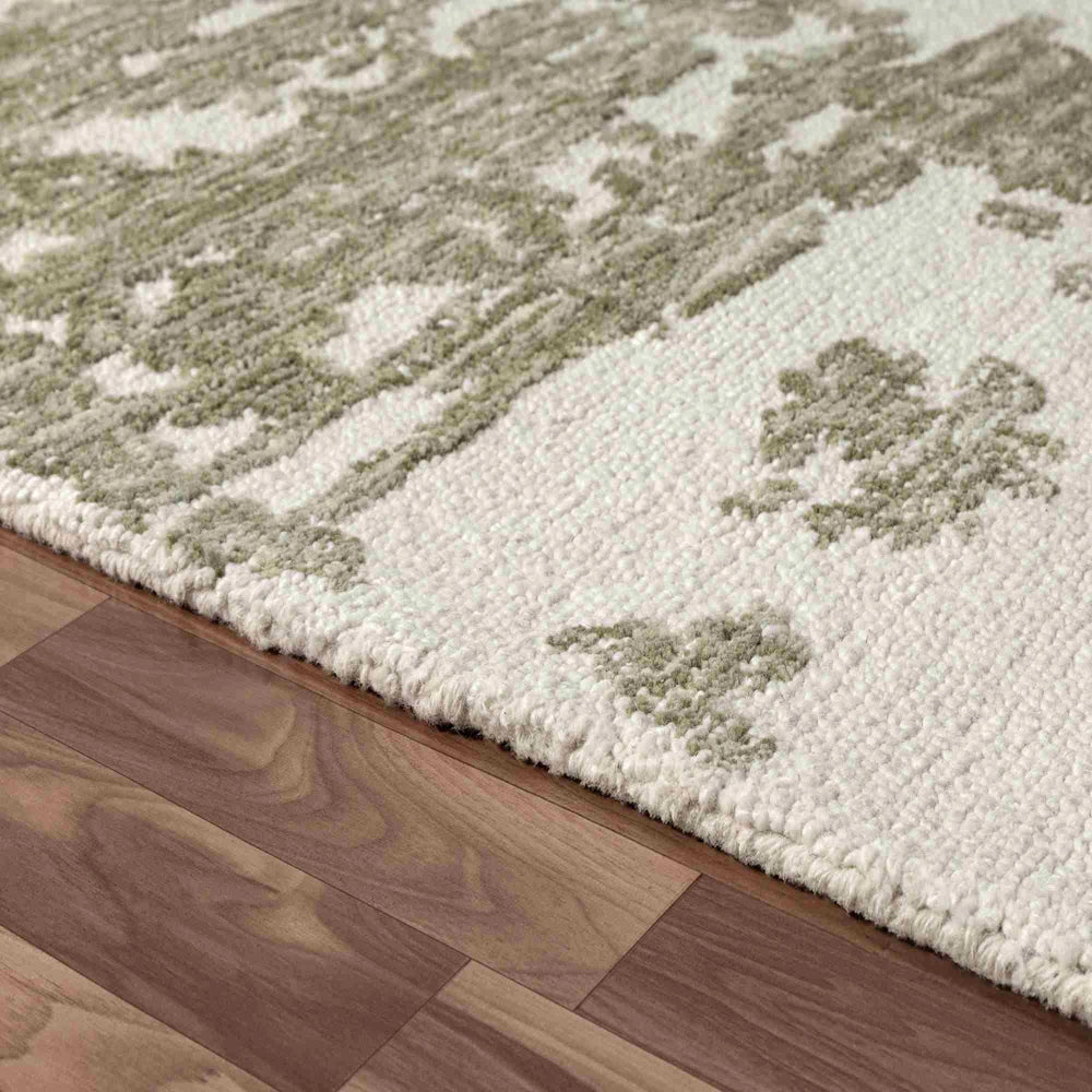Close up of green and ivory hand tufted rug edge with textured abstract pattern and plush looped pile detail.