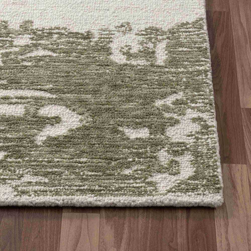 Close up of green and ivory hand tufted rug corner with abstract pattern, textured pile and bound edges.