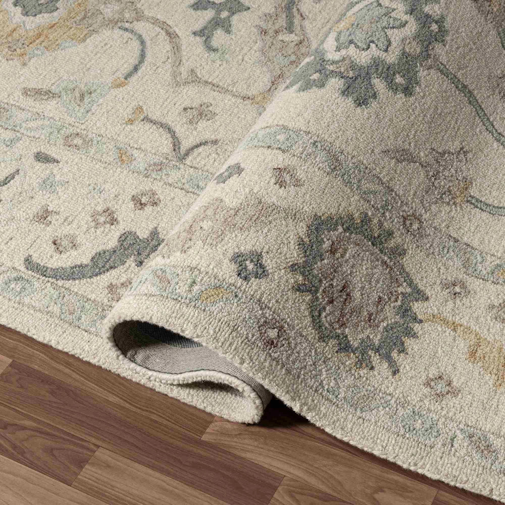 Close-up of a rolled traditional area rug with a beige wool pile and blue floral patterns on hardwood floors.
