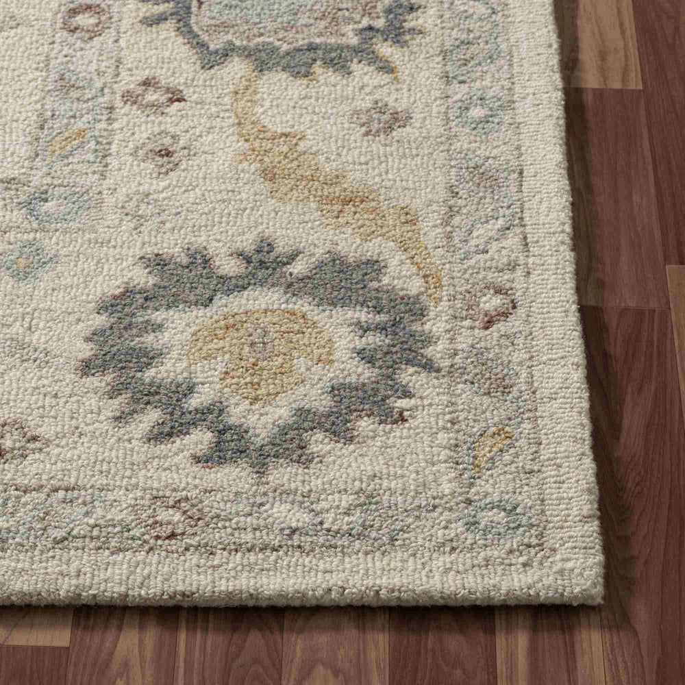 Close-up of a hand-tufted cream rectangle rug with multi-colored floral patterns on hardwood flooring.