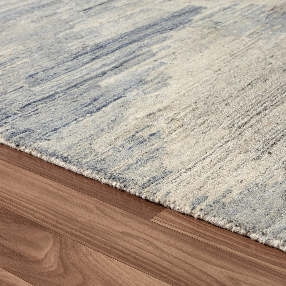 Close up of blue and ivory hand tufted rug edge with abstract striated pattern and soft textured pile detail.