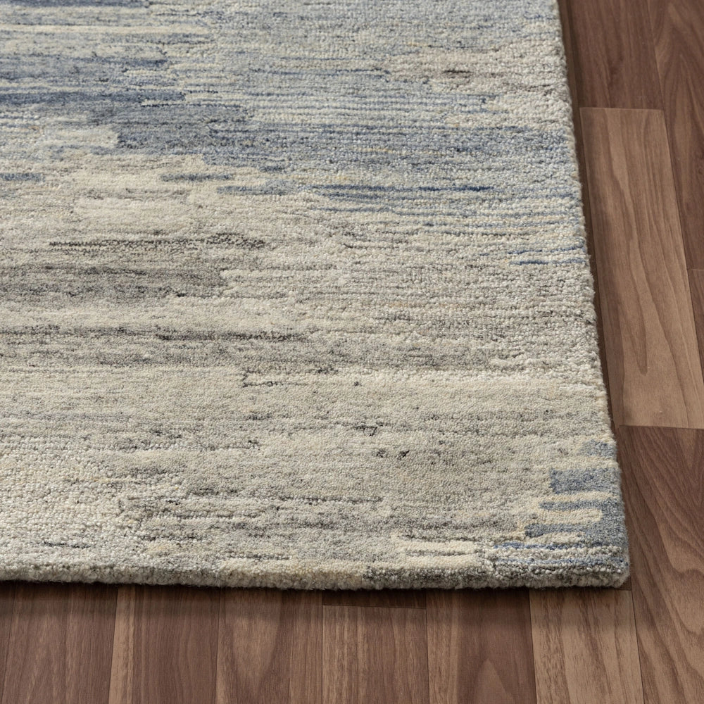 Close up of blue and ivory hand tufted rug corner with abstract striated pattern, textured pile and bound edges.