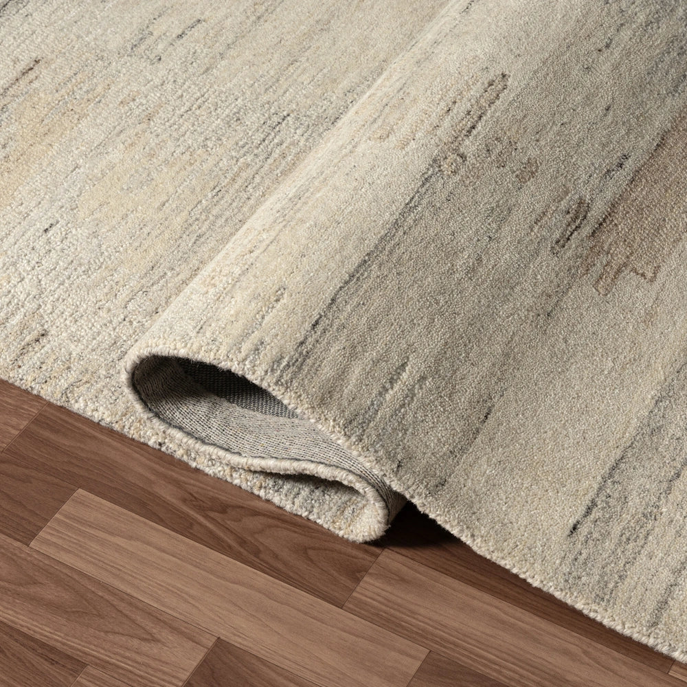 Close up of cream hand tufted rug corner showing soft textured pile, subtle striated pattern and folded edge detail.