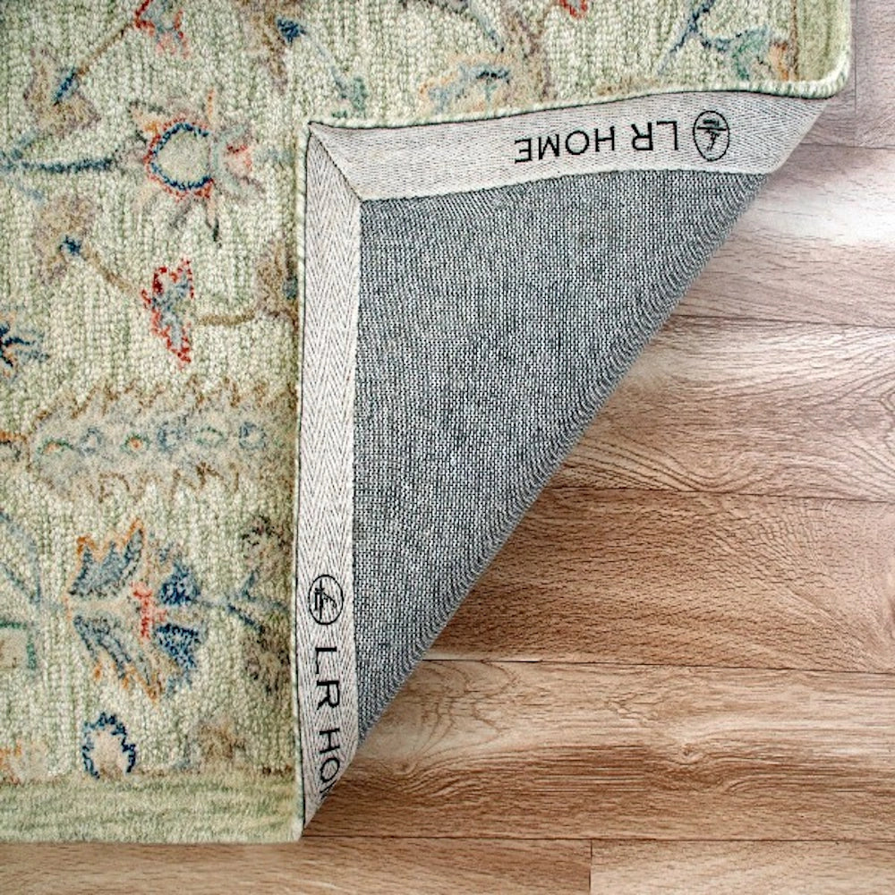 LR Home green floral area rug folded back to show the canvas backing on a light wood floor.