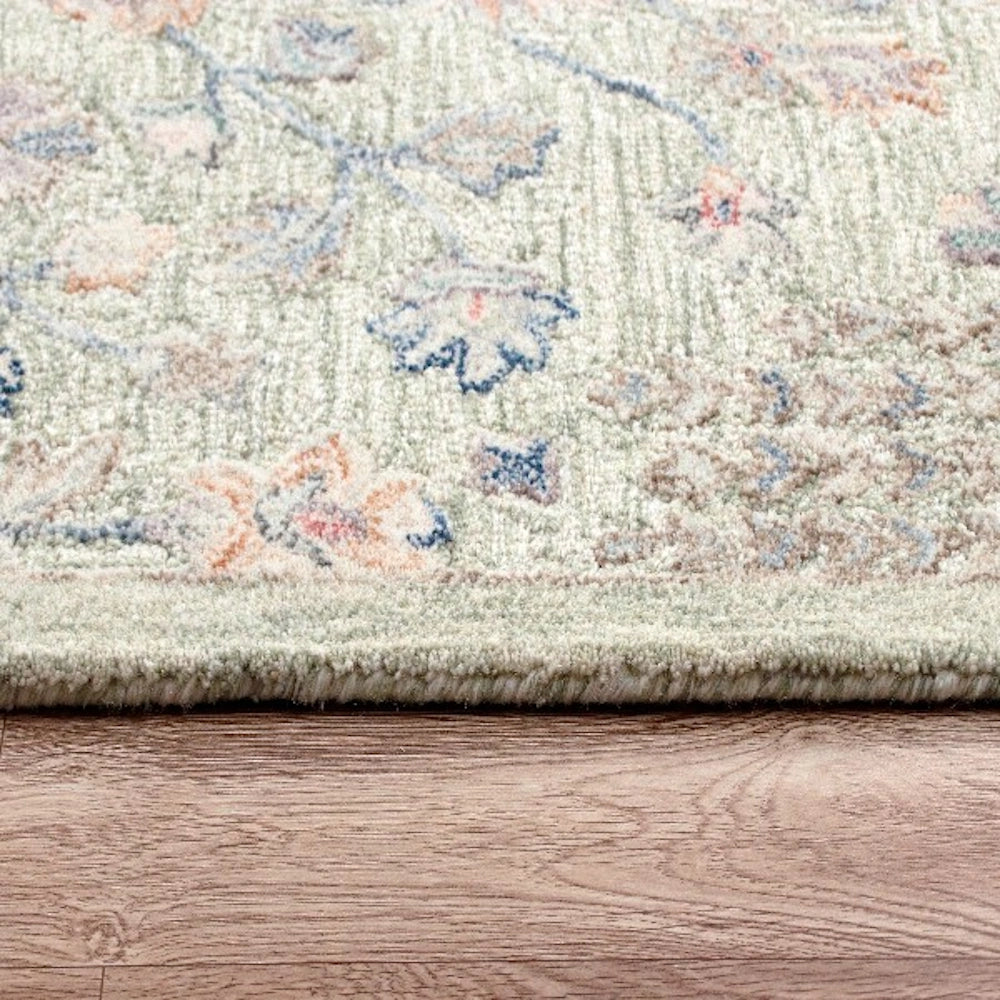 Sage green hand tufted rectangle vintage rug with floral patterns on a wooden floor.