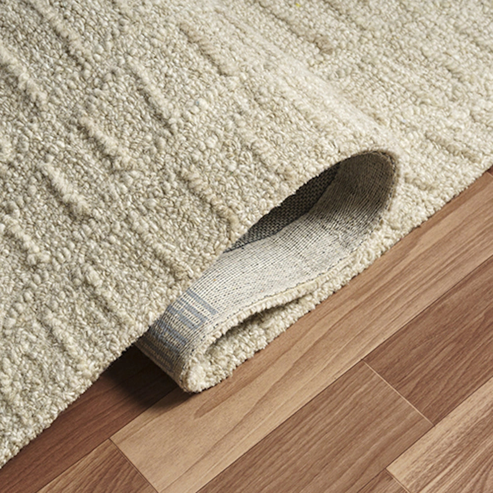Hand tufted rectangle haze rug showing textured weave pattern and backing on hardwood floor.