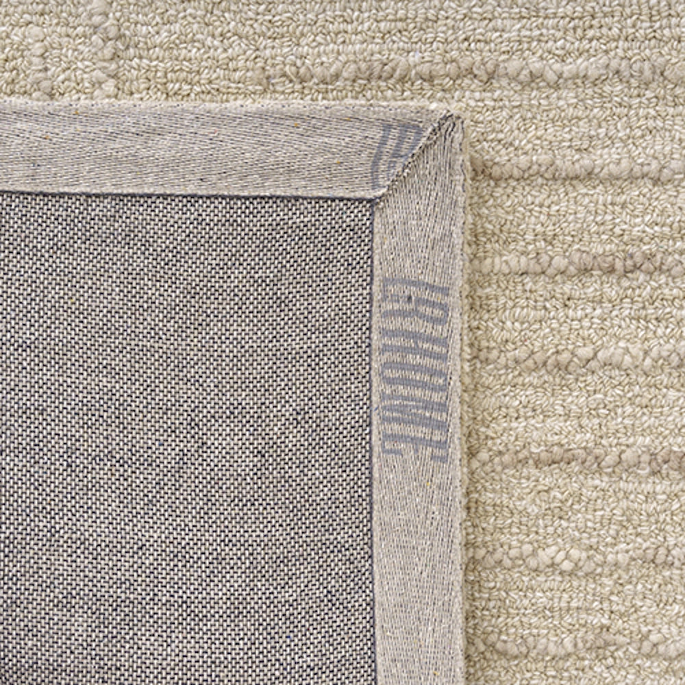Close-up of the non-slip canvas backing and stitched border corner of a textured beige wool area rug.