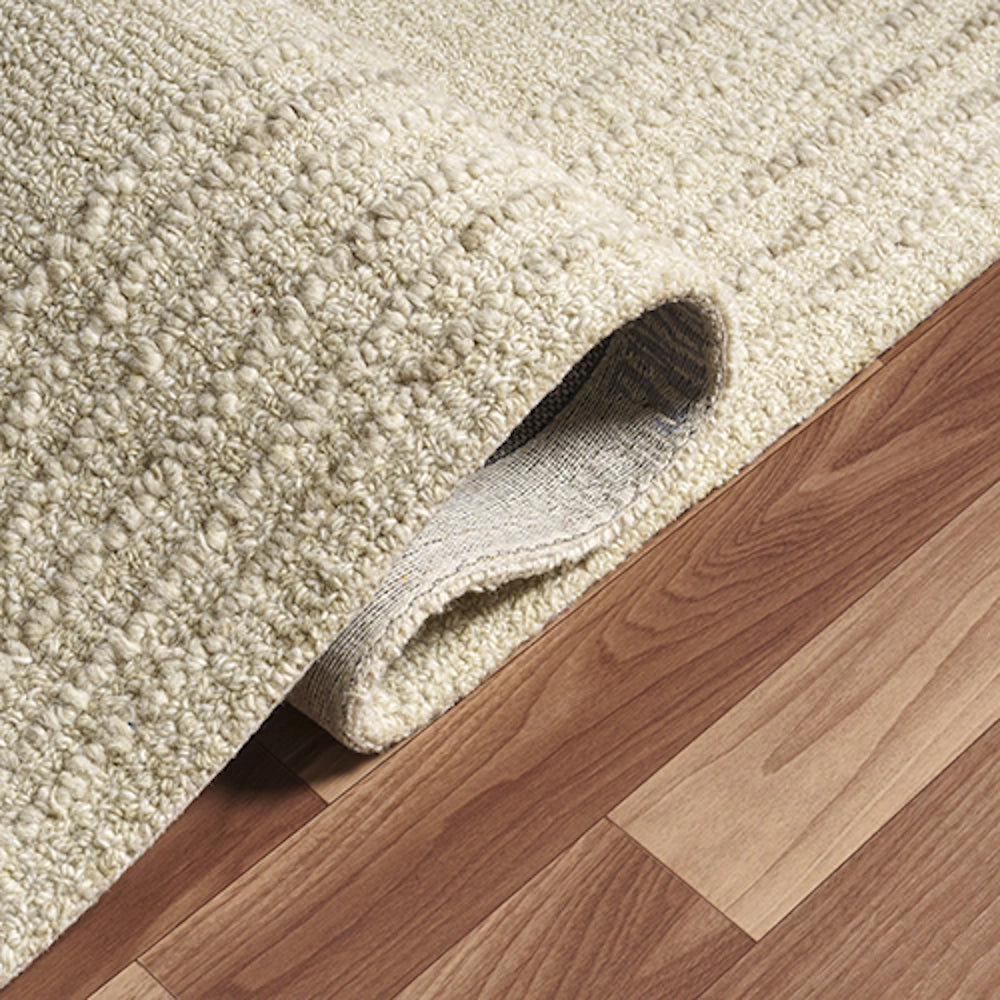 Hand-tufted rectangle haze oatmeal rug showing texture, corner folded back on hardwood floor.