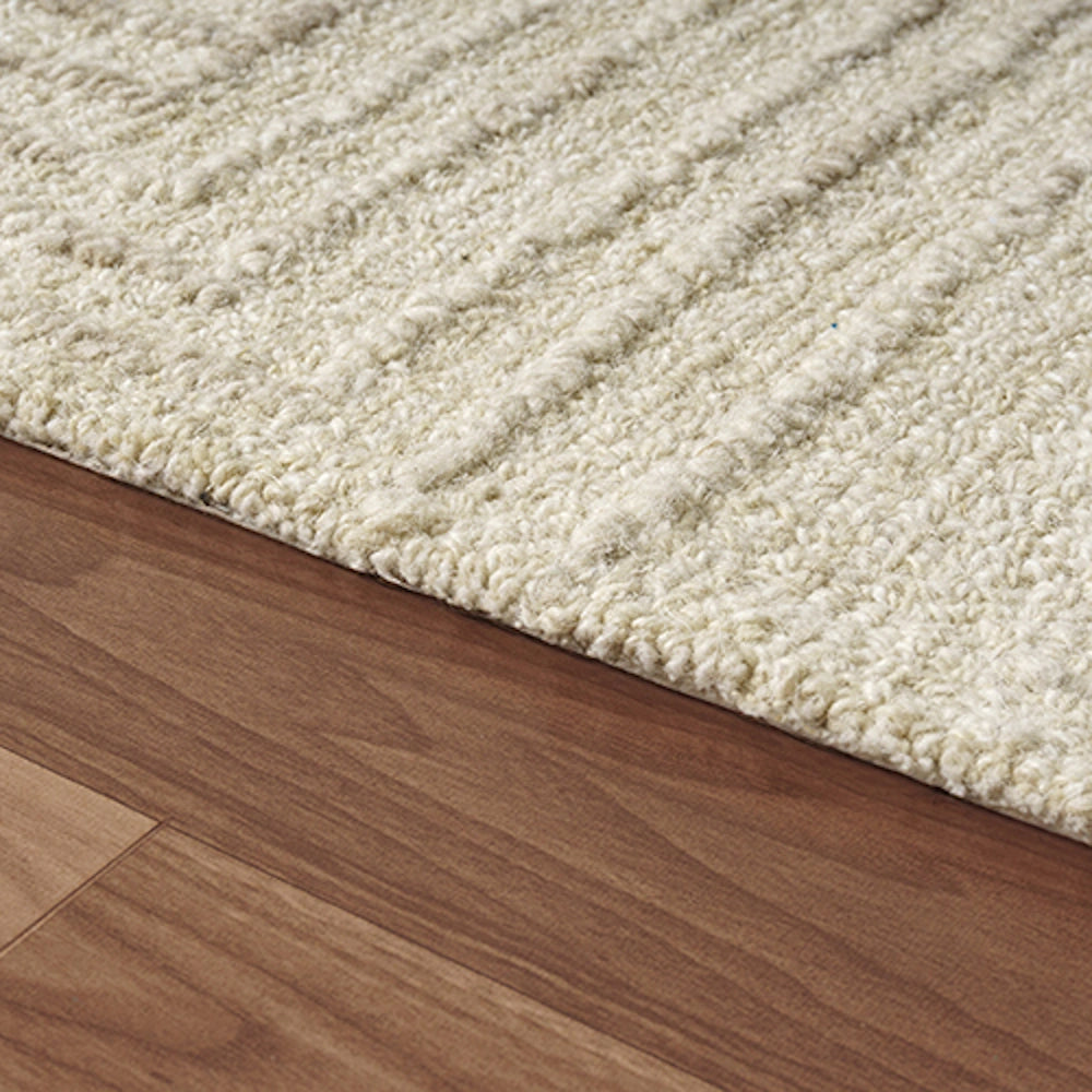 Close up of an oatmeal hand tufted rectangle haze rug showing its textured pile on a hardwood floor.