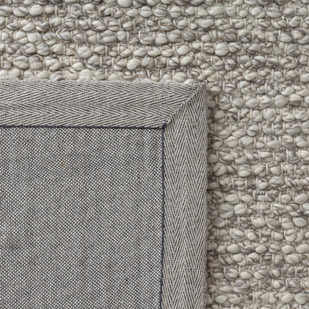 Chunky loop wool rug corner showing cream bobble texture and grey mitered herringbone canvas backing.