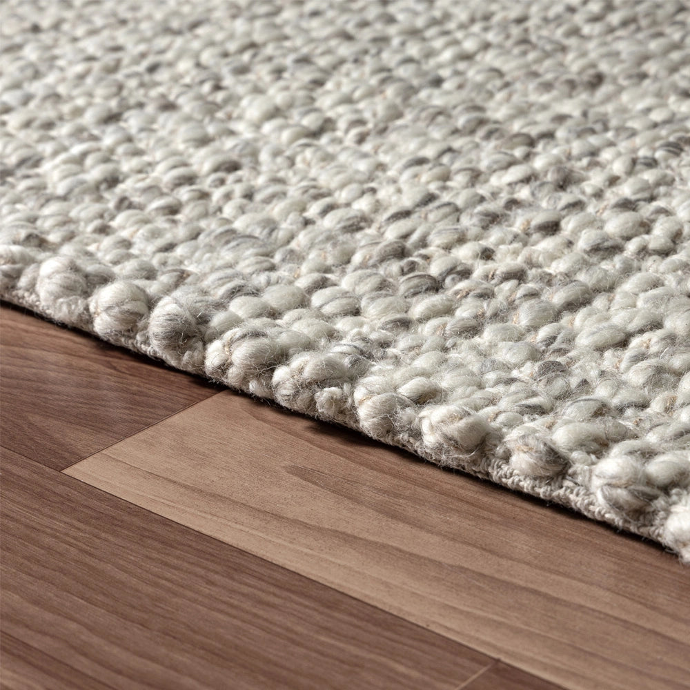 Hand-woven textured grey and white rectangle dome rug on a brown wooden floor.