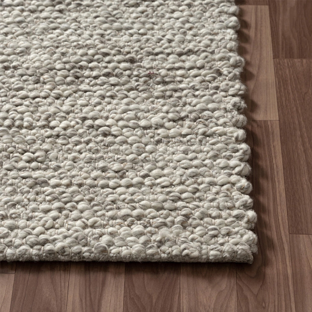 Close-up of a chunky hand-woven wool dome rug in grey on a hardwood floor.