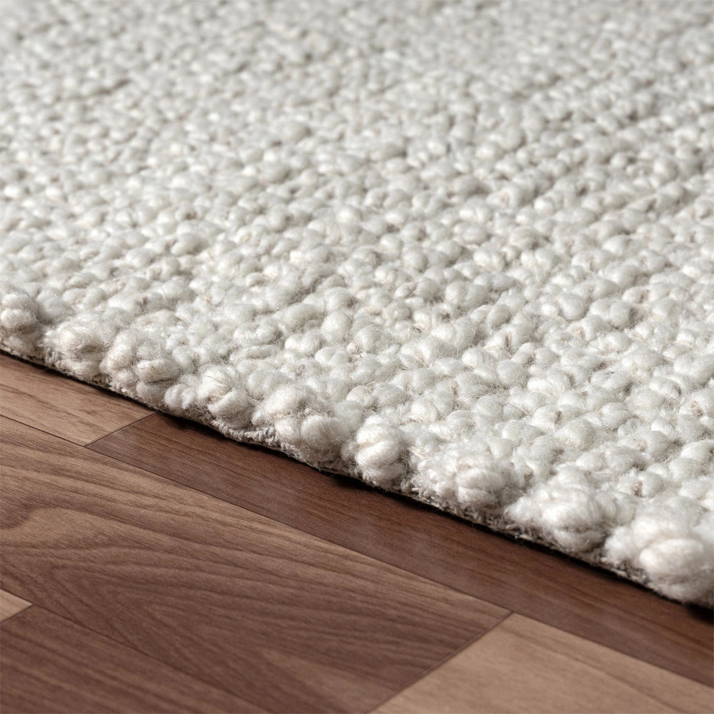 Close-up of a textured white wool loop area rug on a dark hardwood floor.