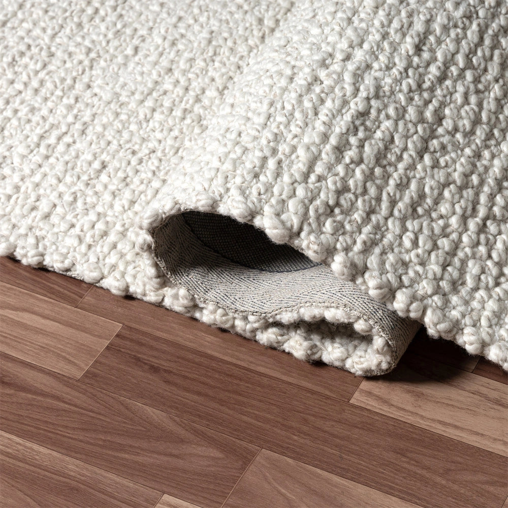 Thick textured cream wool rug rolled up on dark hardwood floor, showing backing.