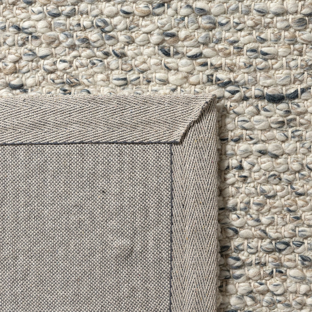 Close-up of a textured cream wool area rug showing its stitched canvas backing and durable corner border.