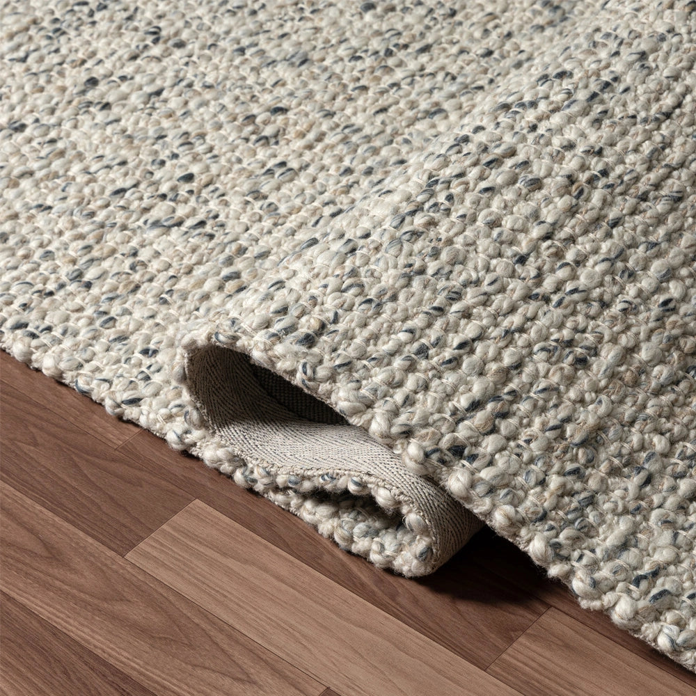 Hand-woven ivory rectangle dome rug with a textured wool weave rolled up on a dark hardwood floor.