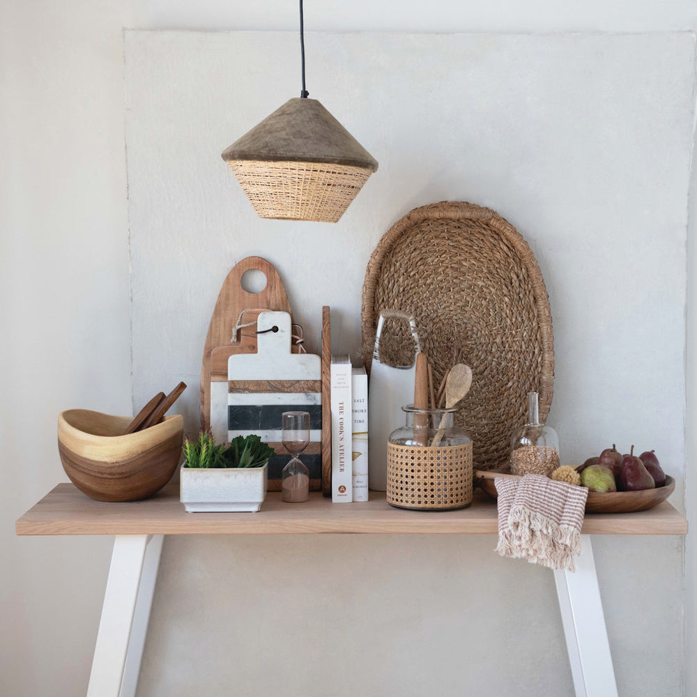 Oval woven seagrass tray displayed on a kitchen counter with cookbooks, wooden utensils, and glass jars.
