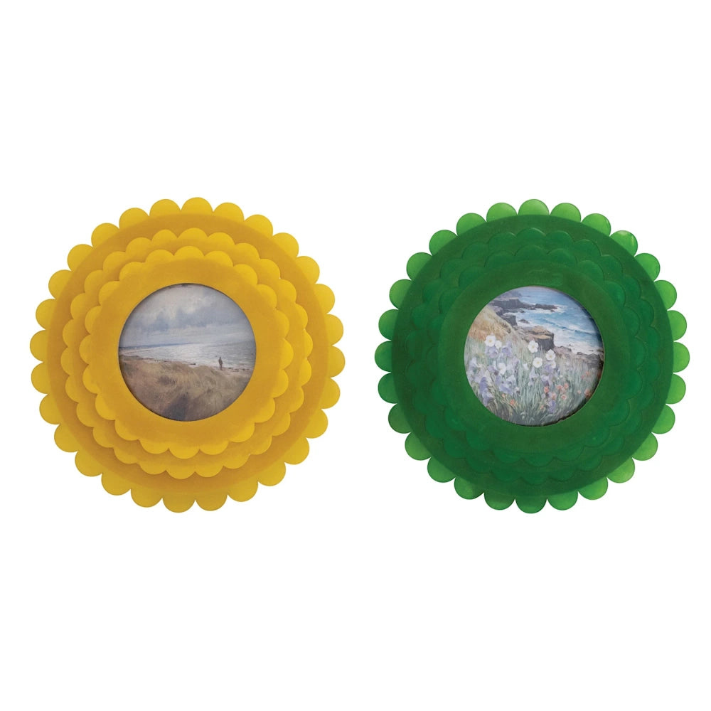 Two round, handmade resin photo frames in yellow and green with scalloped edges, featuring small coastal landscape paintings.