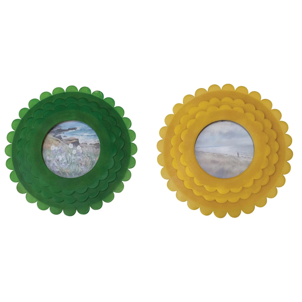 Two round resin photo frames with scalloped edges in green and yellow, featuring coastal landscape and floral art prints.