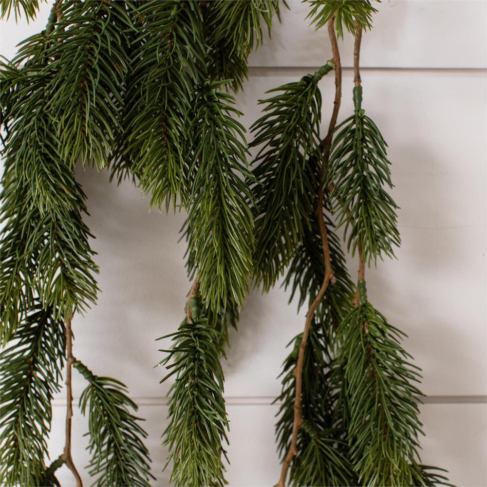 Close-up of vibrant green artificial pine garland hanging against a white paneled wall.